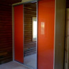 oranžová šatní skříň na míru s posuvnými dveřmi umístěná v rohu